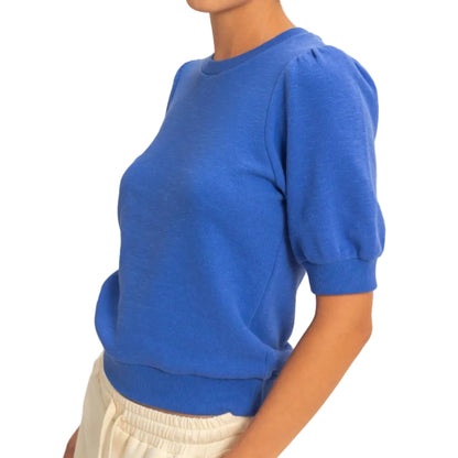 Person wearing a blue sweater and white pants against a neutral background