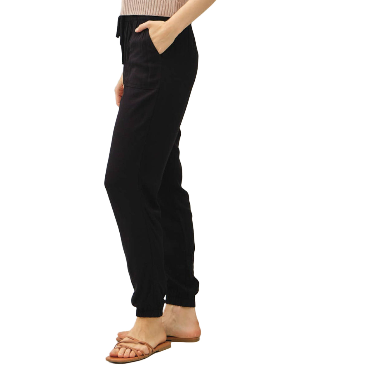 Woman wearing a beige sleeveless sweater and black pants on a white background