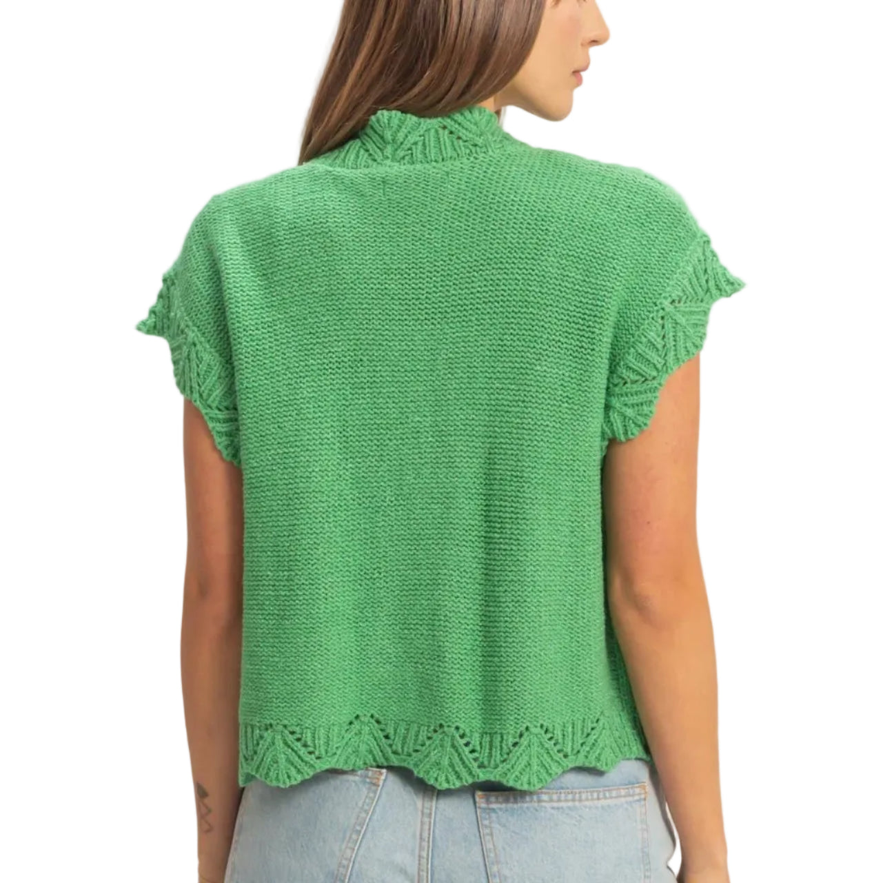 Woman wearing a green knitted top and denim shorts on a plain background
