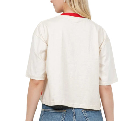 Woman wearing a white shirt and blue jeans standing against a white wall with a plant to the left.