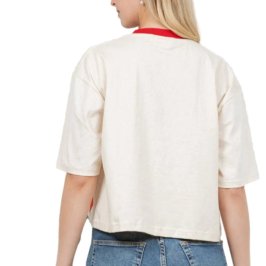Woman wearing a white shirt and blue jeans standing against a white wall with a plant to the left.