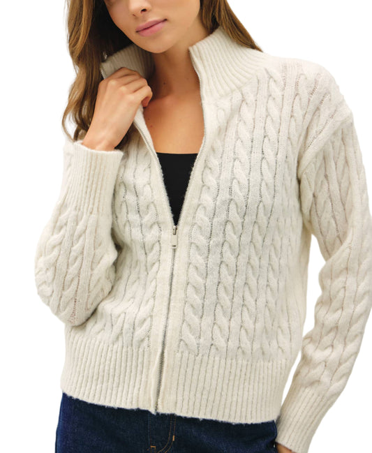 Woman wearing a cream cable knit cardigan against a plain background