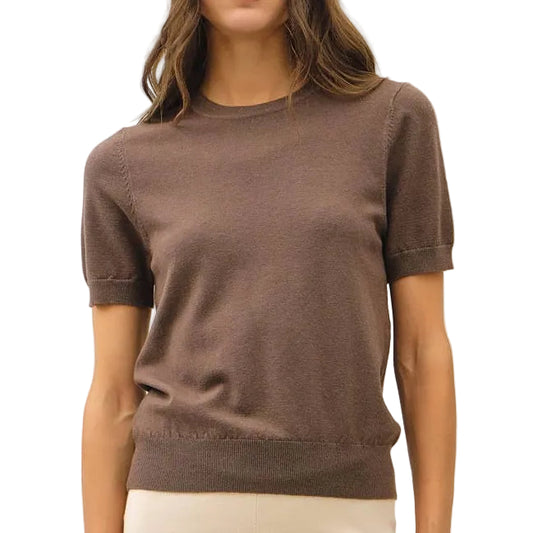 A woman modeling a short-sleeve brown knit top and cream wide-leg trousers with brown shoes, standing against a plain white studio background.
