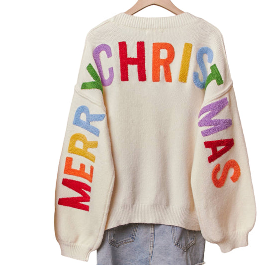 Beige sweater with colorful 'Merry Christmas' text on a hanger against a neutral background.
