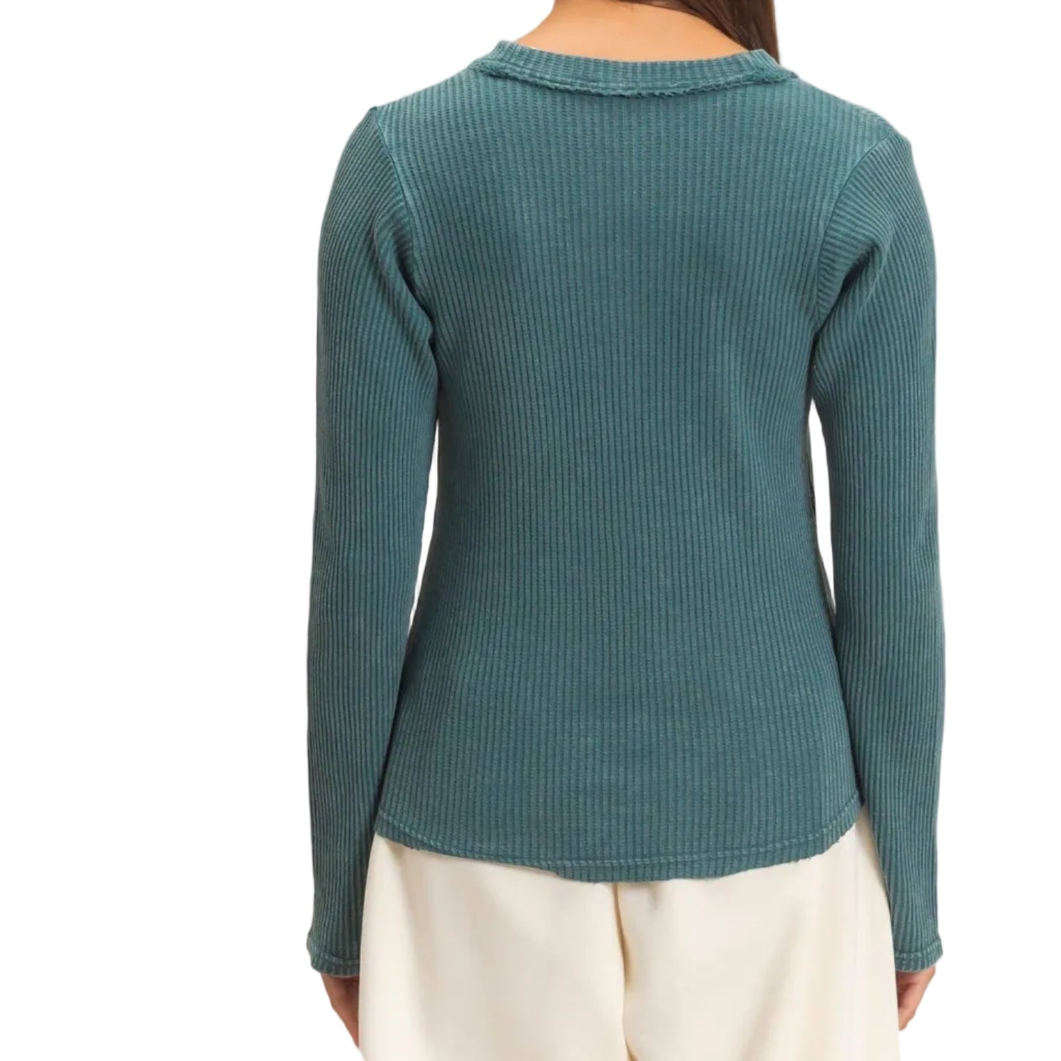 A woman viewed from the back wearing a teal ribbed long-sleeve top and cream pants against a plain beige studio background.