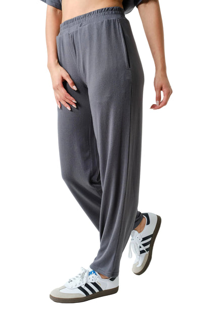 Person wearing gray sweatpants and white sneakers with black stripes on a light background