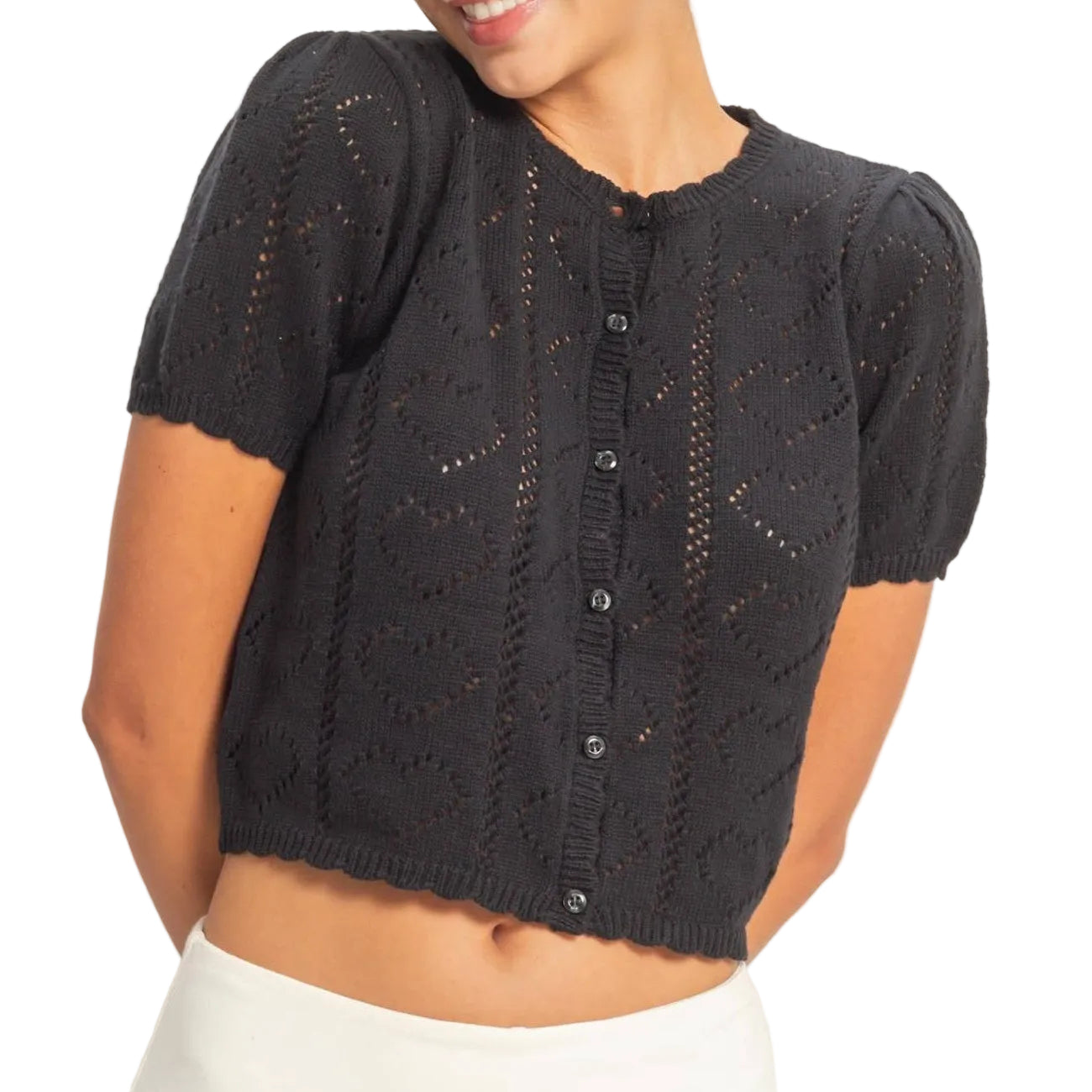 Woman wearing a black knit cardigan over a white top against a plain background