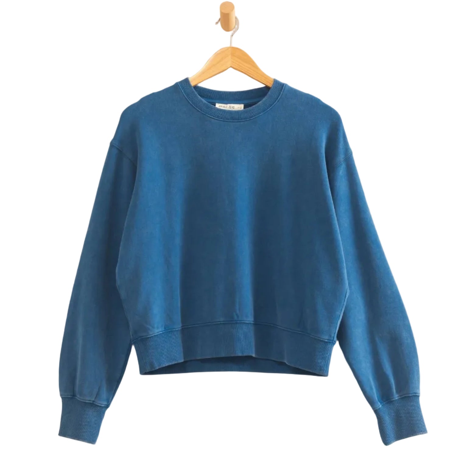 A blue cropped crewneck sweatshirt hanging on a wooden hanger against a plain off-white wall.