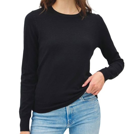 Woman wearing a black long-sleeve top and light blue jeans against a white background