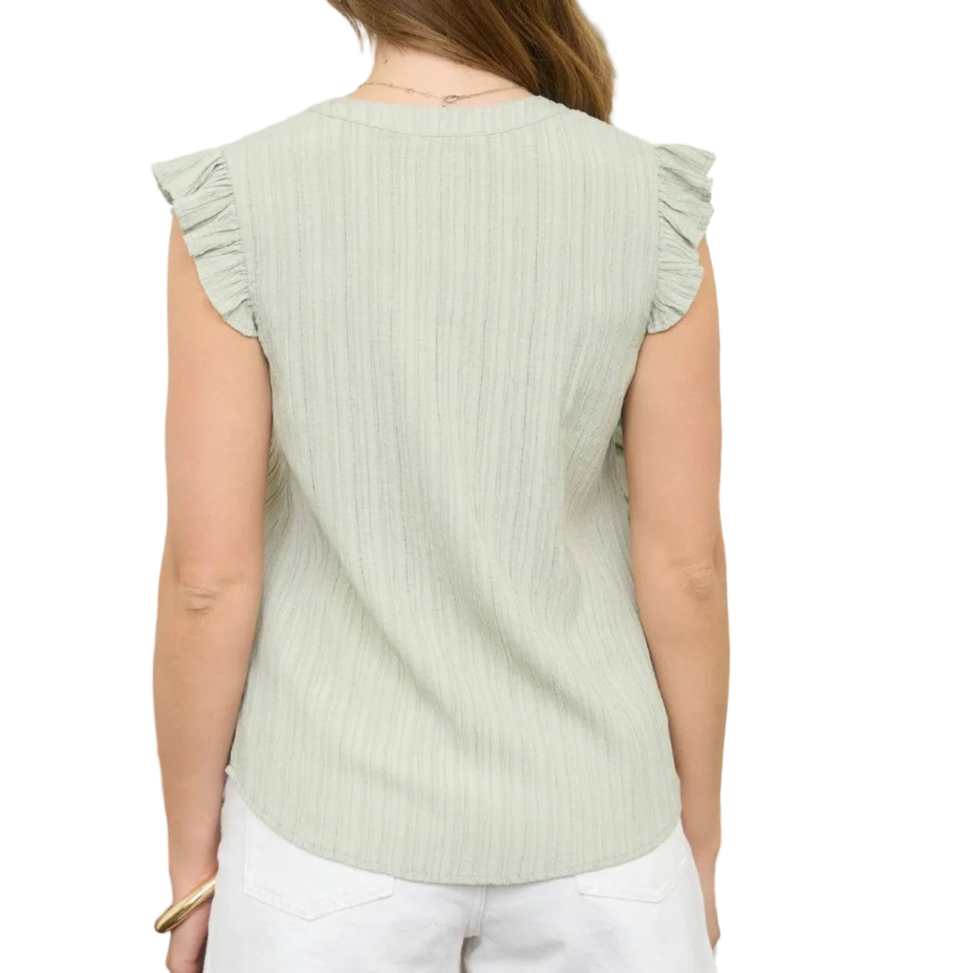 Woman wearing a light green sleeveless top with ruffled shoulders, standing in front of a white wall with plants.