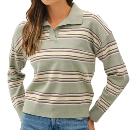 A woman wearing a sage green long-sleeve polo sweater with horizontal stripes in beige, brown, and muted pink, paired with blue jeans, against a plain light gray studio background.