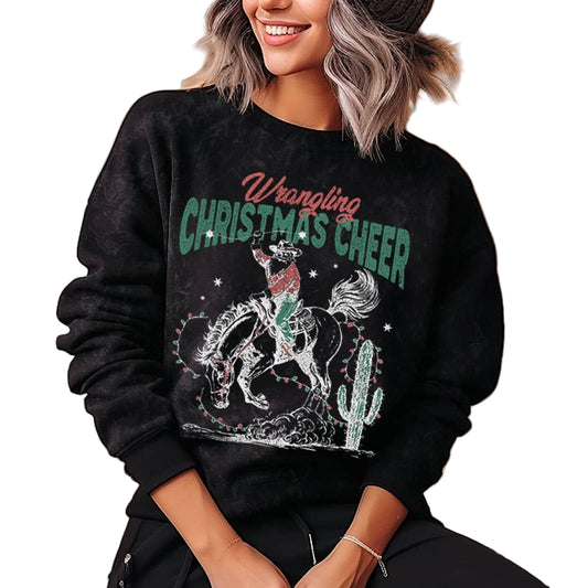 Person wearing a black sweatshirt with 'Wrangling Christmas Cheer' text and graphic, sitting in front of string lights.