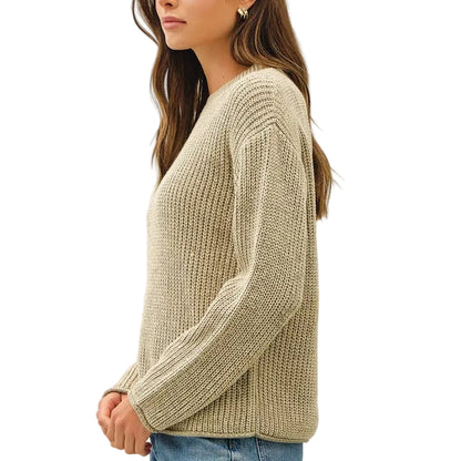 A woman stands in profile wearing a ribbed knit sweater, blue jeans, and brown sneakers against a plain white studio background.