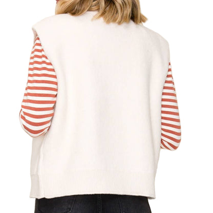 Woman wearing a white sweater with red striped sleeves against a plain background