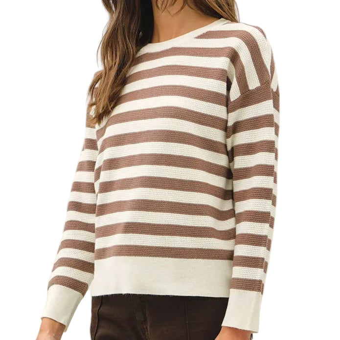 A woman modeling a brown and cream striped knit sweater paired with dark brown wide-leg trousers and tan sneakers, standing against a plain white studio background.