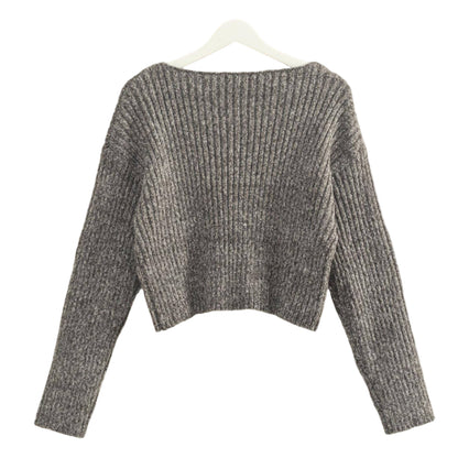 Gray knitted sweater on a hanger against a beige wall