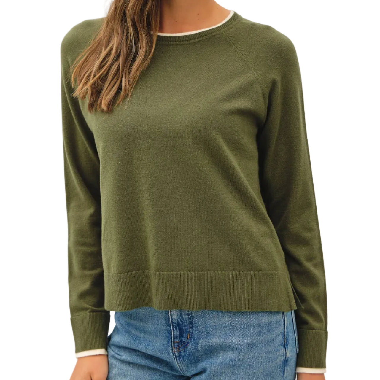 A woman wearing an olive green long-sleeve crewneck sweater with white contrast trim at the collar and cuffs, paired with blue jeans, against a plain light gray background.