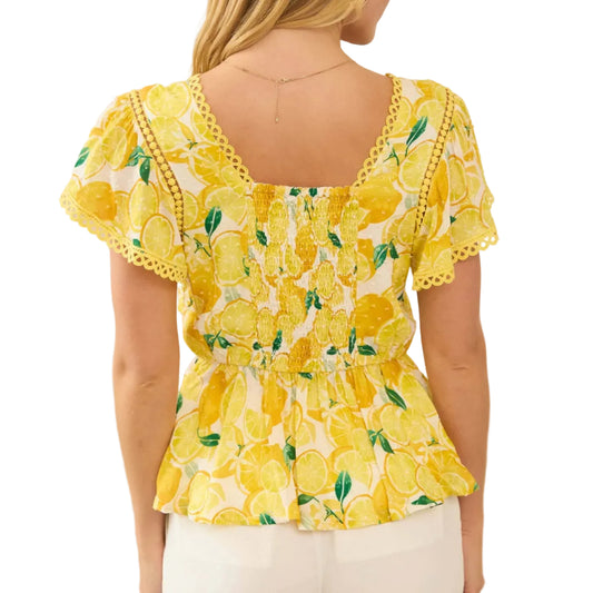 Woman wearing a yellow floral blouse with ruffled sleeves in a neutral setting