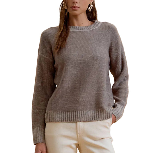 A woman modeling a gray knit crewneck sweater and cream wide-leg trousers against a solid beige studio background.