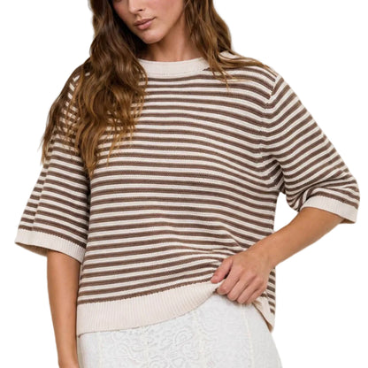 Woman wearing a striped shirt and white pants against a light-colored wall.