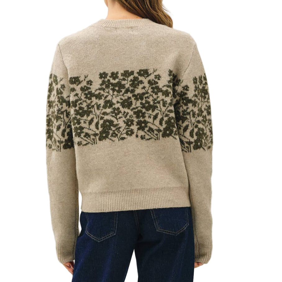 Person wearing a beige sweater with floral patterns and blue jeans on a white background