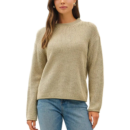 A woman modeling a beige ribbed knit sweater, blue cuffed jeans, and brown sneakers against a plain white studio background.