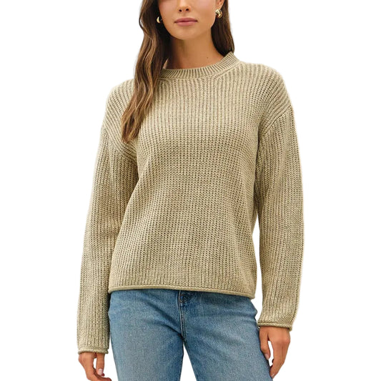 A woman modeling a beige ribbed knit sweater, blue cuffed jeans, and brown sneakers against a plain white studio background.