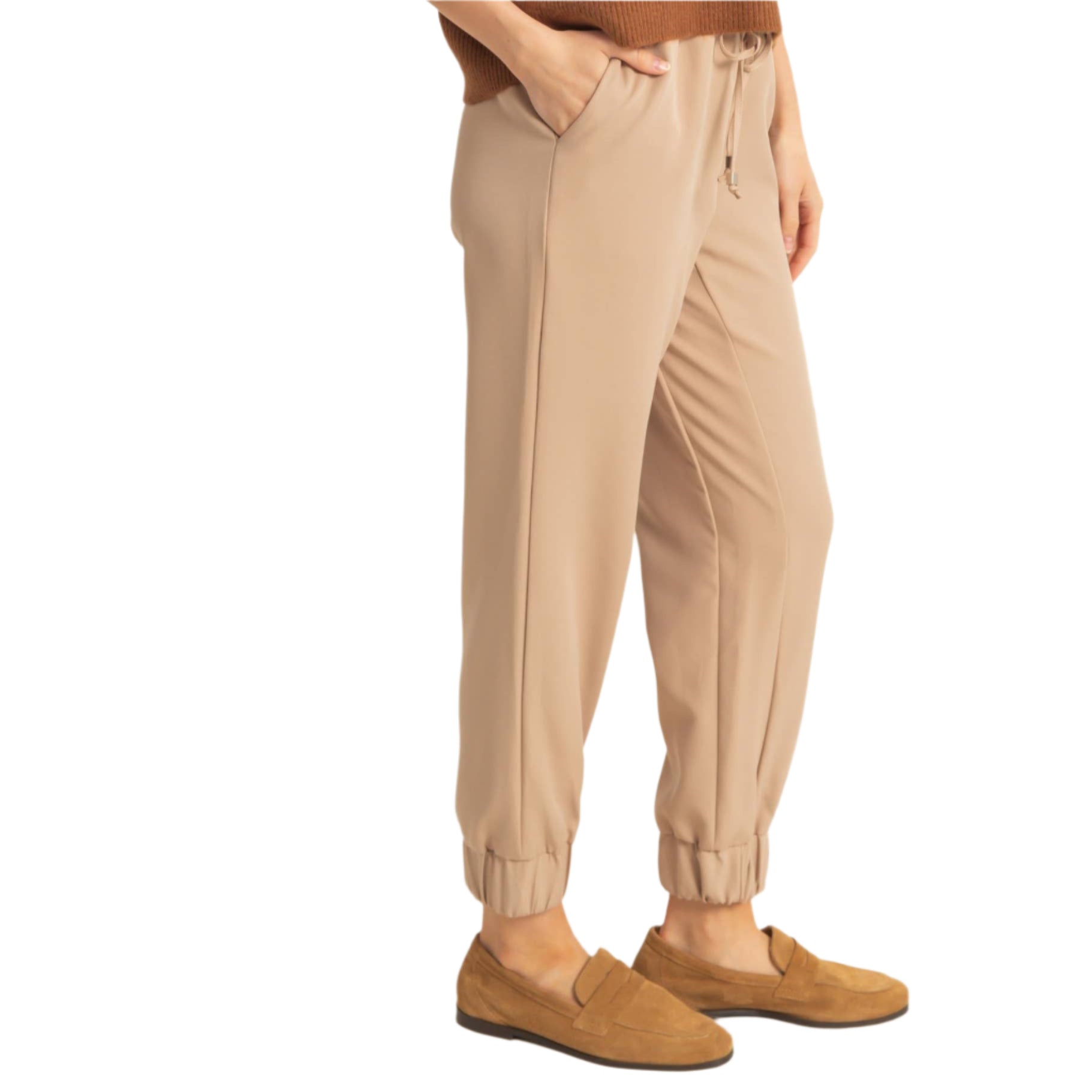 Person wearing beige jogger pants and brown shoes on a plain background