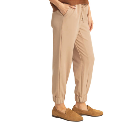 Person wearing beige jogger pants and brown shoes on a plain background