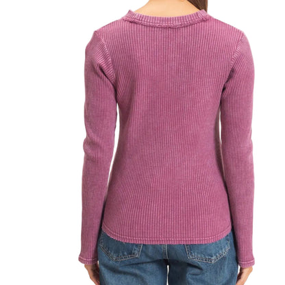 A woman viewed from the back wearing a ribbed long-sleeve knit top in dusty pink and blue jeans, against a plain off-white background.