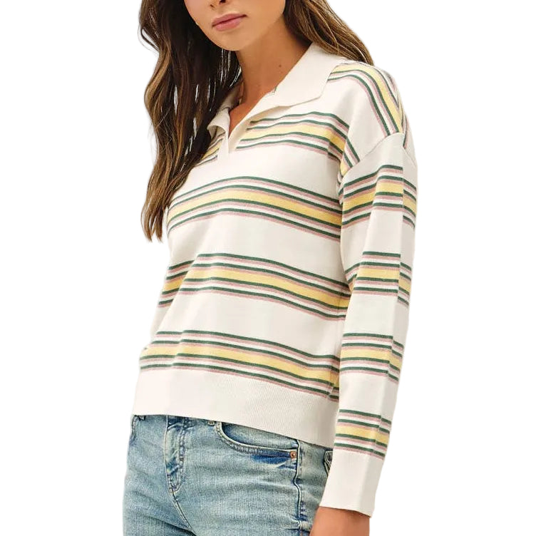 A woman modeling a white long-sleeve knit sweater with thin yellow, green, and blue horizontal stripes, paired with light-wash blue flare jeans and brown shoes, against a plain white studio background.