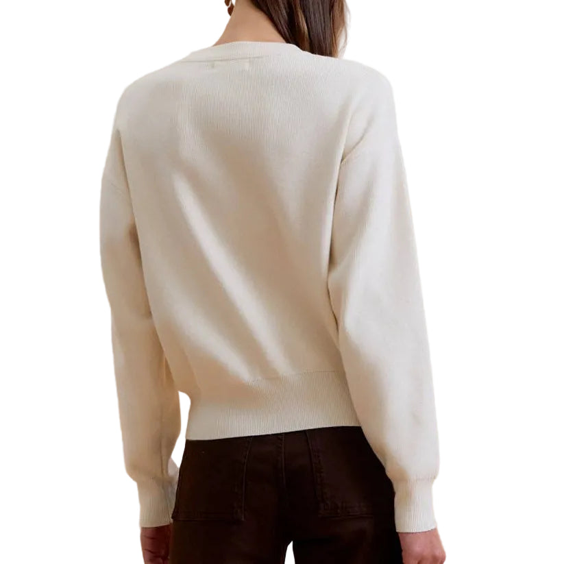 A model shown from the back wearing a cream knit sweater and dark brown wide-leg trousers, standing against a solid beige background.