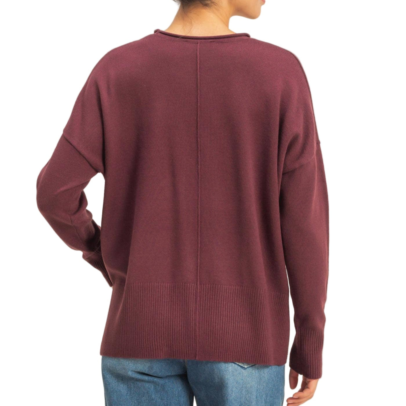 Person wearing a burgundy sweater and blue jeans on a beige background