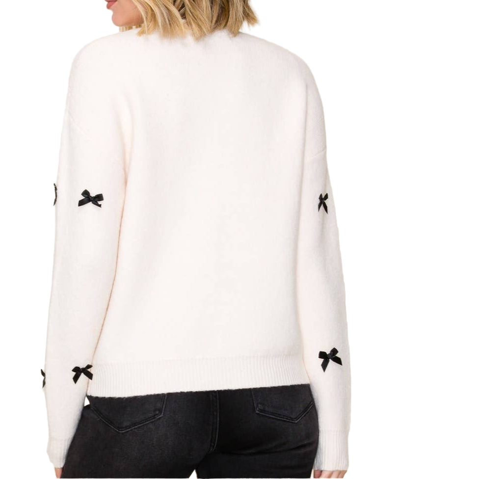 Woman wearing a white sweater with black bow details on a plain background