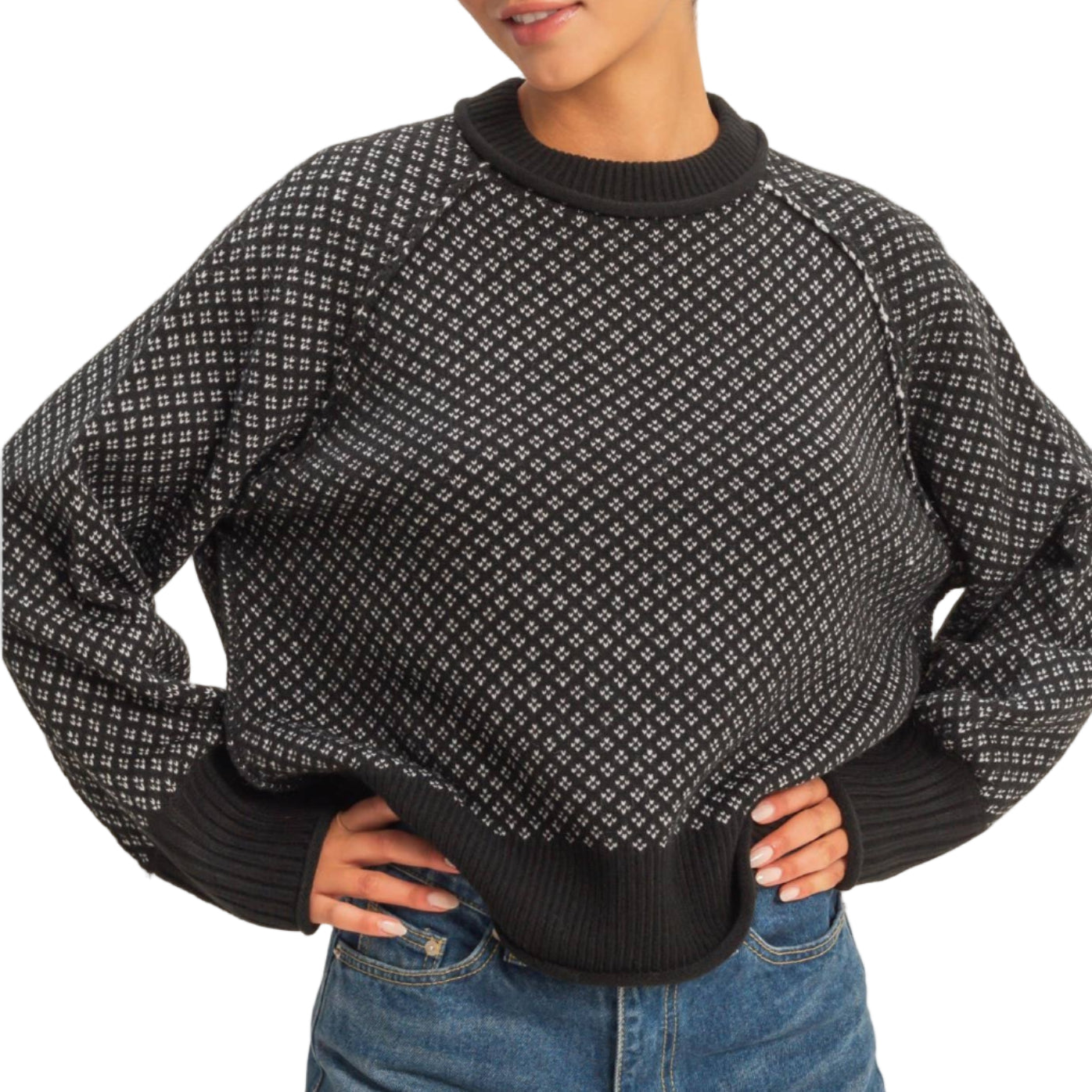 Person wearing a black patterned sweater and blue jeans on a plain background