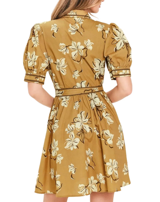 A woman shown from the back wearing a mustard yellow puff-sleeve dress with a cream and brown floral print, set against a plain off-white background.