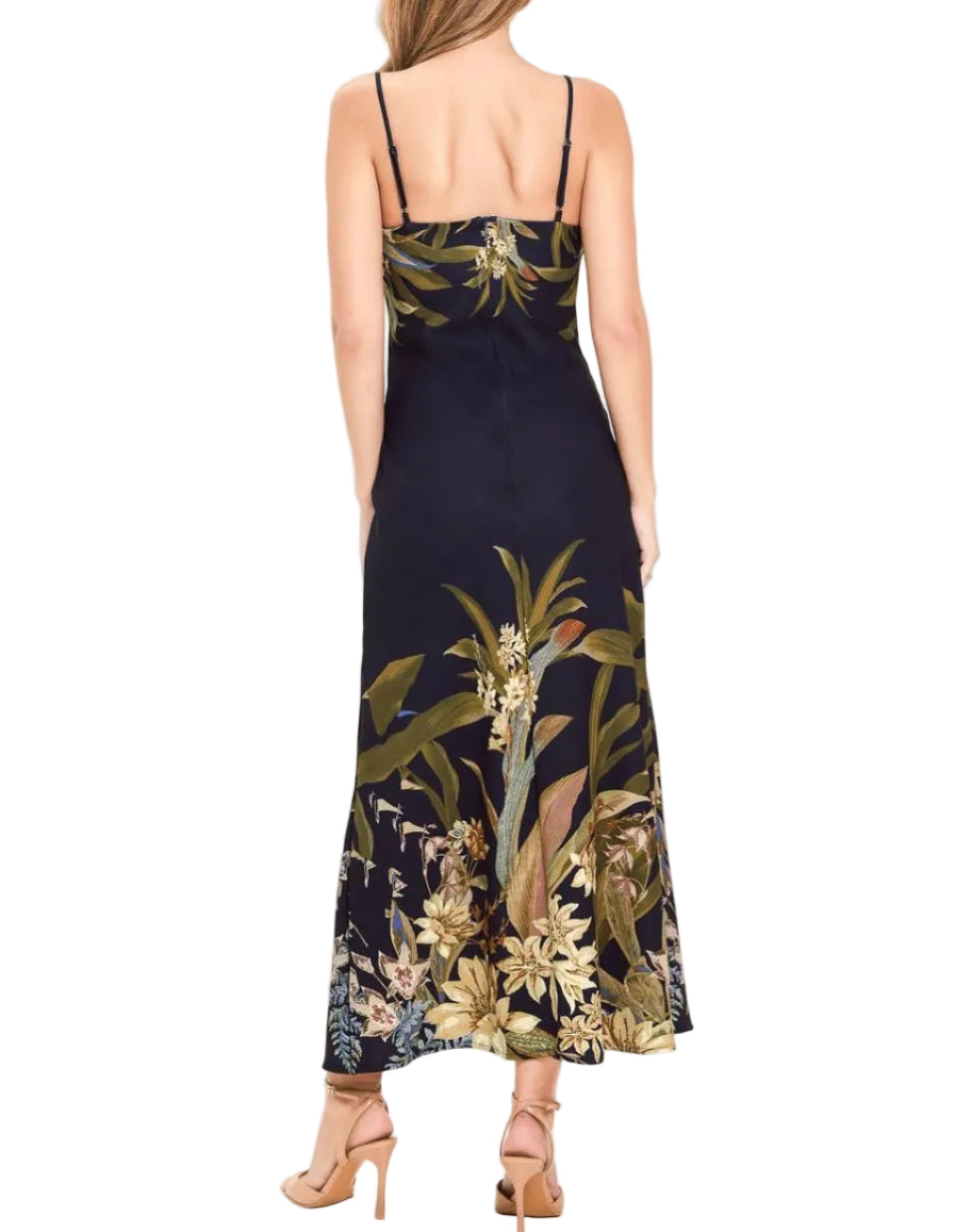 A woman shown from the back wearing a sleeveless maxi dress with thin straps and a dark navy base featuring a large botanical floral print in olive green, beige, and white. She is wearing beige high-heeled sandals against a plain white studio background.