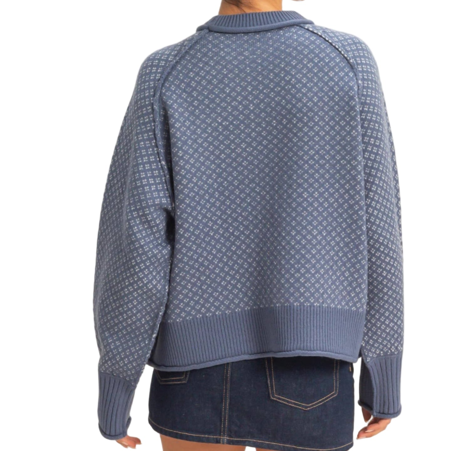 Person wearing a blue patterned sweater and denim skirt on a plain background