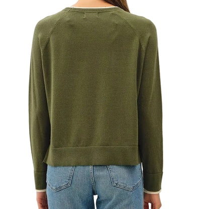 A woman viewed from behind wearing an olive green long-sleeve knit sweater, light blue cropped jeans, and tan slip-on shoes against a plain off-white studio background.