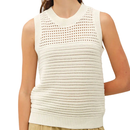Woman wearing a white sleeveless knitted top against a plain background