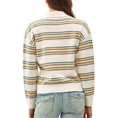 A woman viewed from behind wearing a cream-colored knit sweater with yellow and blue horizontal stripes, paired with light-wash blue jeans and tan shoes, against a plain white studio background.
