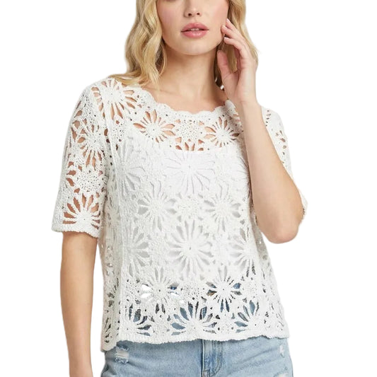 Woman wearing a white lace top and denim shorts on a light pink background