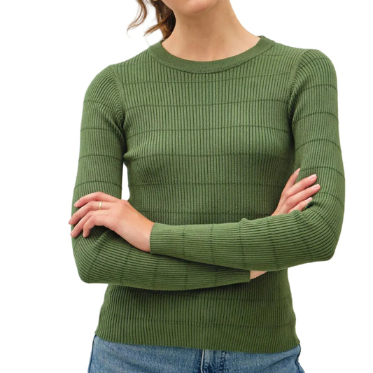 A woman wearing a ribbed knit crewneck sweater in olive green, paired with blue jeans, standing against a plain light gray background.