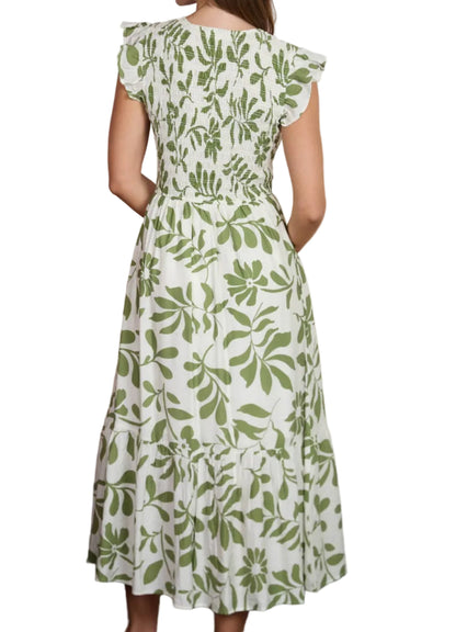 Woman wearing a green and white floral dress standing by a blurred beach scene.