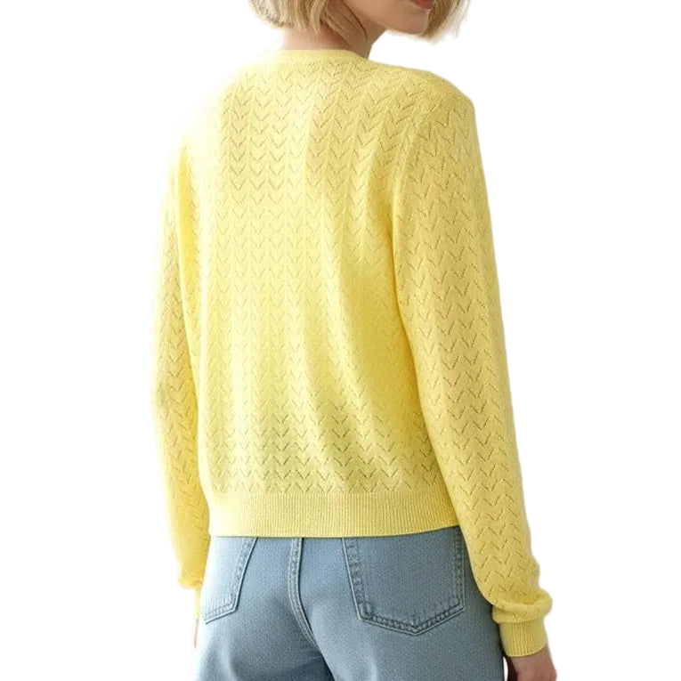 Woman wearing a yellow sweater and denim shorts standing by a window with a plant in the background